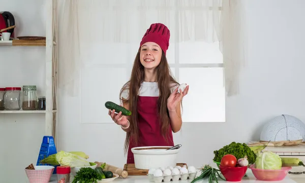 Mat i din budget. Ung kock matlagning med gurka och ägg. barn förbereda hälsosam mat hemma och bär kock uniform. städning och hemhjälp. Utveckling av barndomen. liten flicka bakning — Stockfoto