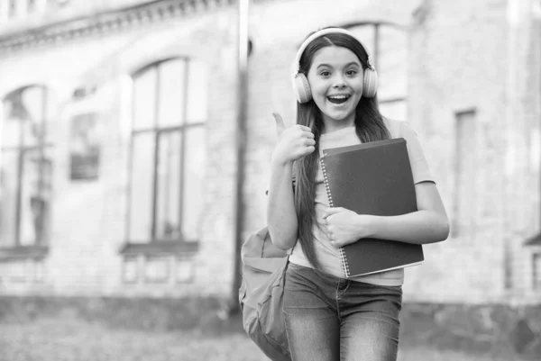 子供のための教育。音楽を聴いてる。幸せな子供時代。女の子はヘッドフォンをしてる。現代の教育技術です。陽気な女の子はフォルダを保持します。学校に戻って。ノート付きの幸せな子供 — ストック写真