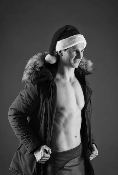 Atletický muž se šesti balení abs nosit Santa klobouk a teplý kabát s kožešinovou kapuci pro pobyt stylový v chladném období červené pozadí, zima — Stock fotografie