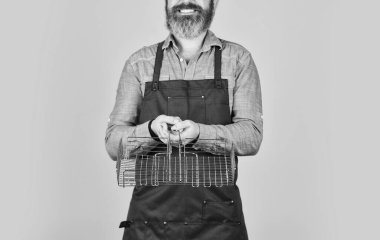 Sağlıklı yemek yapmak. Barbekü ızgarası önlüklü adam. Mutfak konsepti. Kızarmış et için aletler. Mutfak aletleri. Şef bbq yemeği pişiriyor. Yaz pikniği. Hippi sakalı, bbq ekipmanlarını tanıtıyor.