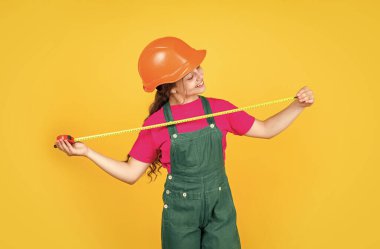 Zeki profesyonel. Bina ve inşaat. Onarım konsepti. Küçük kız mezura kullanıyor. Mühendis. Mutlu çocuk mezurası. Çocuk müteahhit kask takıyor. Şapkalı ve üniformalı genç kız.