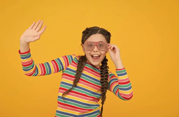 Счастливая девочка с плетеными волосами носить радужный цвет и гламурные очки партии на желтом фоне, счастливое детство — стоковое фото