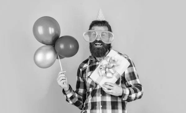 Snygg skäggig kille med trendig frisyr bära rutig skjorta hålla fest ballonger och nuvarande låda, lycka — Stockfoto