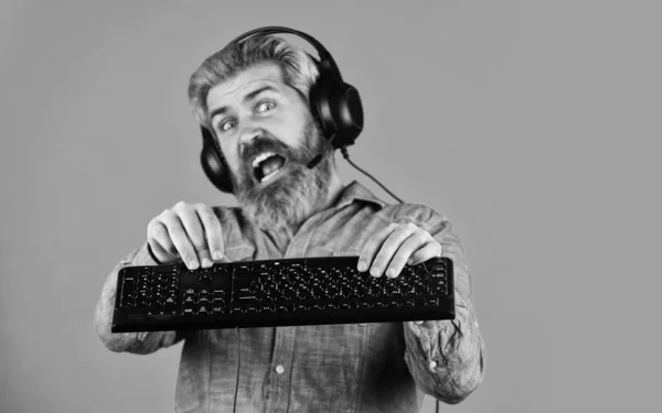 Une performance supérieure. Paramètres graphiques poussés à la limite. Jouer à des jeux informatiques. Homme barbu hipster gamer écouteurs et clavier. Dépendance au jeu. Jeux en ligne. Loisirs modernes. Exécuter un jeu moderne — Photo