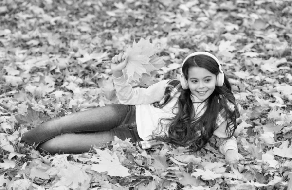 Jour d'automne parfait de joyeux enfant écouter du livre audio ou de la musique portant des écouteurs dans le parc de la saison d'automne jouer avec des feuilles d'érable jaune tombé, la musique — Photo