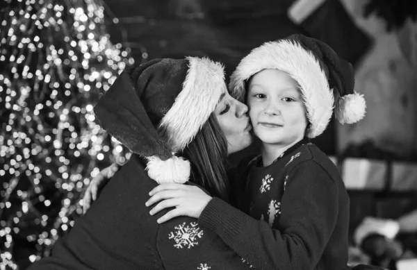 A hagyományunk. A kisfiú szereti az anyját. Karácsonyi buli. Anya és a gyerek télapó sapkát és pulcsit viselnek. megosztani ajándékokat és ajándékokat rokonokkal. Anya és fia ünneplik a karácsonyt. családi nyaralás ideje — Stock Fotó