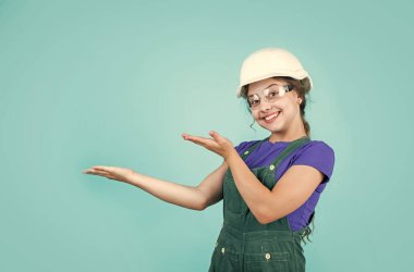 Müstakbel mühendis ürünü sunacak. Onarım için güvenlik gözlüğü takan mutlu bir çocuk. İnşaat alanı. Çocuk mimar. İşçi bayramı. Çocukluk gelişimi. Genç kız asistanı