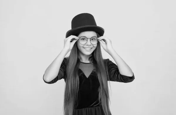 Feliz bebé pequeño usar sombrero negro en el pelo largo morena fijación gafas de moda con aspecto de fiesta fondo amarillo, vista — Foto de Stock