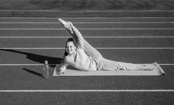 Девочка тренировки спорта снаружи на стадионе арене раскол на коврик для йоги, здравоохранение — стоковое фото