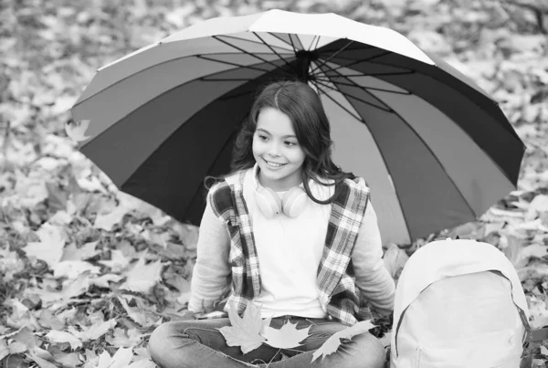 Perfecto día de otoño de niño alegre bajo paraguas colorido con bolsa de la escuela sentado en el parque de temporada de otoño disfrutando del buen tiempo con hoja de arce, tiempo lluvioso — Foto de Stock