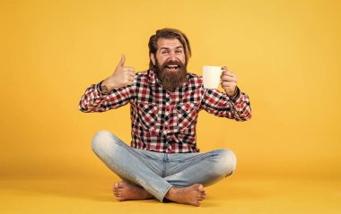 Bunu dene. Adam fincandan sıcak çay içiyor. Günaydın. Enerjik, sıcak bir içecek. İlham için kahve. Güne mükemmel bir başlangıç. Mutlu sakallı adam sabah kahvesini içiyor. En iyi tat için başparmağınızı kaldırın
