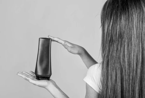 Kid girl with long straight hair hold conditioner shampoo or gel bottle, hair health — Stock Photo, Image