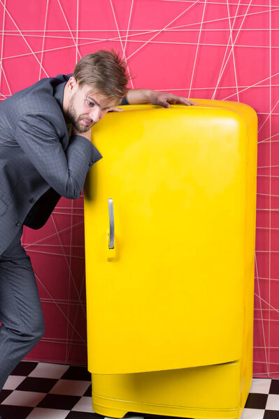 Мужчина формальный элегантный костюм стоять рядом с ретро винтажный желтый холодильник. Винтажные бытовые приборы. Голодные холостяки думают, что едят возле холодильника. Яркий холодильник бытовой техники. Голод и аппетит
