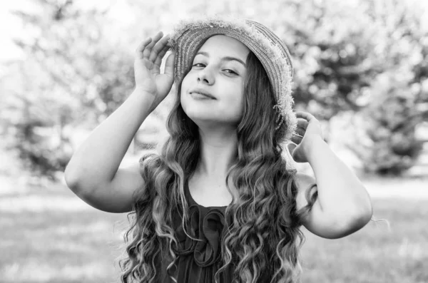 Menina pequena com cabelo ondulado longo e olhar de beleza corrigir chapéu de sol de moda na paisagem ensolarada de verão, fashionista — Fotografia de Stock