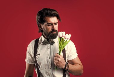 Bahar çiçeği hediyesi. Askılı ve papyonlu romantik bir adam. Kendine güvenen ve zarif bir adam lale çiçekleri tutar. Aşk randevusu için hediye. Buketli eski moda sakallı hippi.