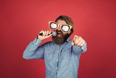 Olgun sakallı adamın uzun saçları var. Parti gözlüğü takıyor ve mikrofonla şarkı söylüyor.