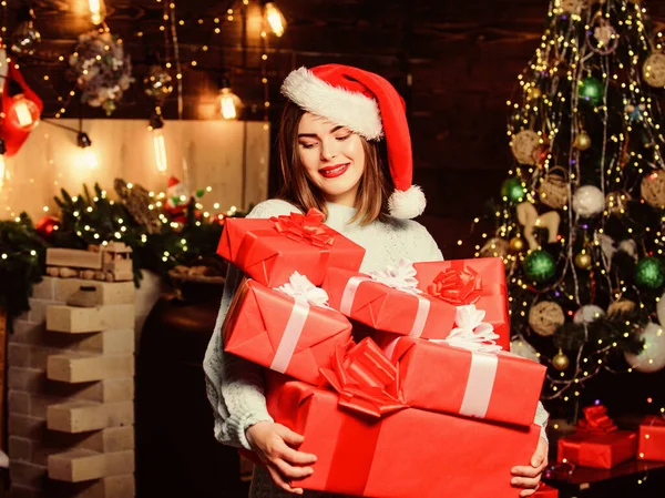 Vrouwe Kerstman viert thuis kerst. Meisje stijlvolle make-up rode lippen bevatten veel kerstcadeaus. Gezellige kerstsfeer. Vrouw kerstman hoed op kerstavond. Breng magie in iemand anders zijn leven. — Stockfoto