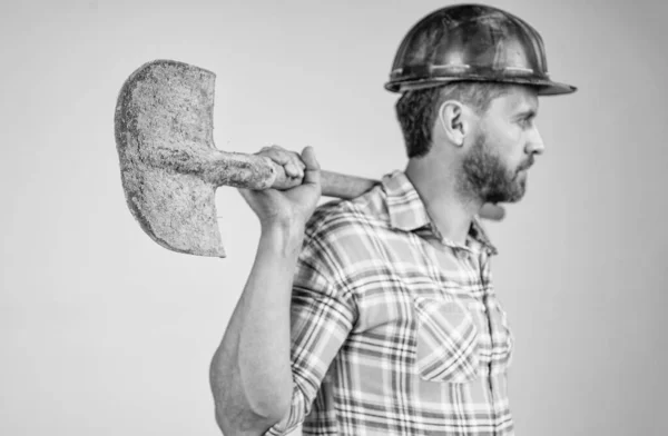 Schep in de hand van een arbeider. Hij draagt een arbeidersuniform. knappe bouwer in helm. — Stockfoto