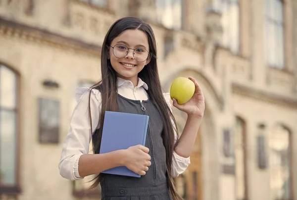 Estou a adorar. Criança feliz segurar maçã e livro. Um lanche da escola. Pausa para lanches. Alimentação saudável e lanches. Comida vegetariana. Dieta e dieta. Pequeno-almoço ou almoço. Educação nutricional. Seja nutritivo — Fotografia de Stock