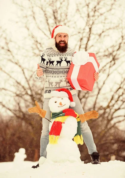 Menschengemachter Schneemann. Der Weihnachtsmann hat Spaß im Freien. Guy glücklich Gesicht schneebedeckten Natur Hintergrund. Hipster mit Bart halten Geschenkbox. Überraschungskonzept. Winterspiele. Winteraktivität. Winterurlaub — Stockfoto