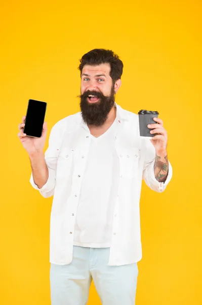 Härligt tillfälle. morgonrutin. Glad skäggig man som håller telefonen medan han dricker kaffe. Brutalt hipster dricker hämtmat från muggen. kille med skägg och mustasch visar mobiltelefon — Stockfoto