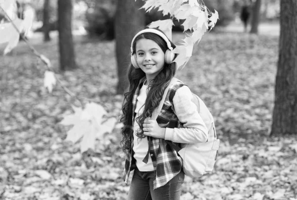 Miúdo no parque de Outono. criança feliz anda entre folhas de outono. menina pequena usar fones de ouvido. de volta à escola. educação moderna. criança com mochila escolar na floresta de outono. conceito de dia de conhecimento — Fotografia de Stock