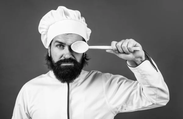 Mannelijke chef-kok in hoed met baard en snor op rode achtergrond gebruik houten keukengerei, koken — Stockfoto