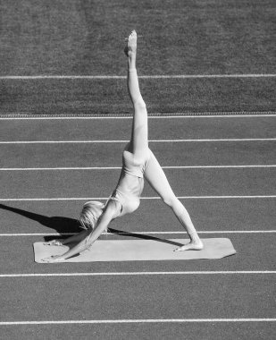 Spor giyimli kadın antrenman öncesi stadyum koşu pistinde yoga yapıyor, pilates yapıyor.