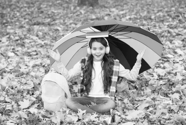 Criança outono sob guarda-chuva. Leia o livro. infância feliz. de volta à escola. menina no fone de ouvido com mochila relaxar no parque. desfrutar de queda na floresta. ouvir música. cursos online educação — Fotografia de Stock