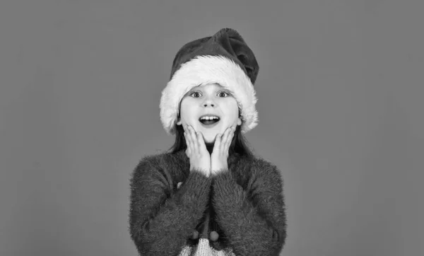 Sorpresivo inesperado. amor vacaciones de invierno. en el estado de ánimo de Navidad. El pequeño ayudante de Santa muestra el pulgar hacia arriba. niña santa claus sombrero fondo rojo. listo para la fiesta de año nuevo. navidad mis vacaciones favoritas —  Fotos de Stock