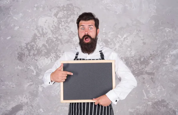 Ώριμος τύπος με γενειάδα και μουστάκι είναι επαγγελματίας σεφ αποδείξει μενού μαγειρικής σε καφέ σε άδειο πίνακα, υπηρεσίες εστίασης — Φωτογραφία Αρχείου