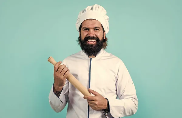 Gelukkig guy chef in hoed met baard en snor op blauwe achtergrond gebruik rollende pin, culinair — Stockfoto