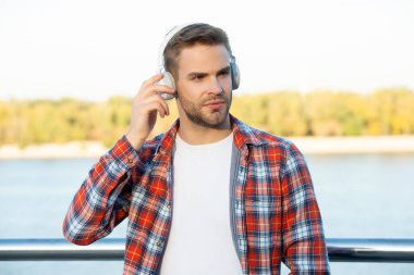 Kareli gömlekli yakışıklı, traşsız adam kulaklıkla müzik dinliyor, modern hayat.