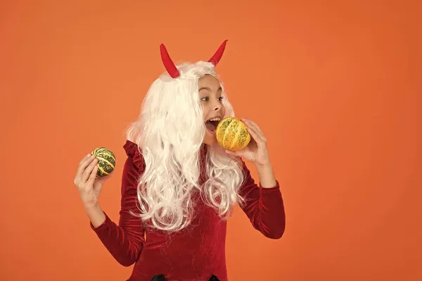 Dziecko nosić diabeł rogi mając długie siwe włosy peruka czuć głód i jeść halloween dyni, szczęśliwy halloween — Zdjęcie stockowe