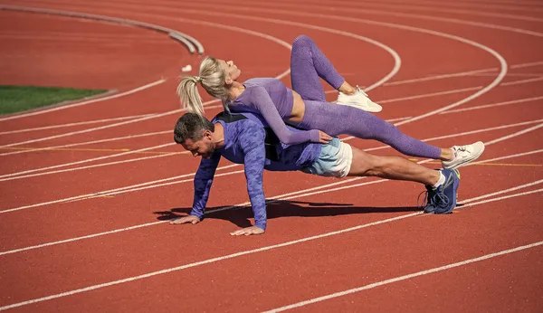 Προπόνηση ζευγάρι γυμναστικής μαζί σταθεί σε σανίδα και να κάνει push up σε υπαίθριο γήπεδο racetrack φορώντας αθλητικά ρούχα, τον αθλητισμό και τη δύναμη — Φωτογραφία Αρχείου