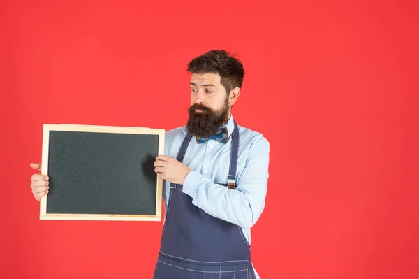 Berber önlüklü ciddi sakallı adam berber dükkanı tahtası kırmızı arka plan fotokopi alanı, okul — Stok fotoğraf