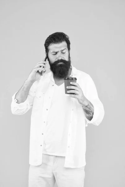 Homme barbu sérieux parlant au téléphone tout en buvant du café, routine du matin — Photo