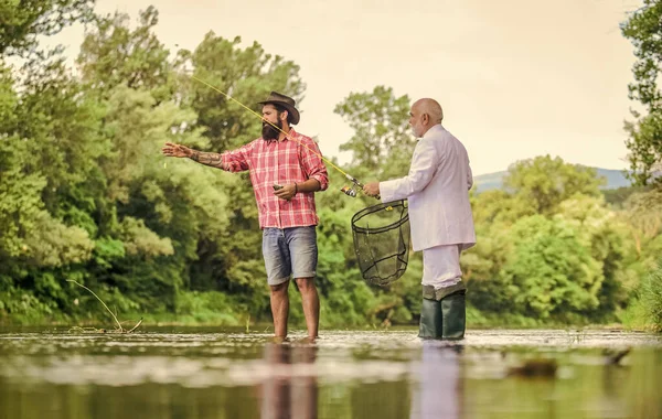 Pescado con acompañante que ayuda en caso de emergencia. Barbudo hombre elegante hombre de negocios pescado juntos. Aprende a pescar. Pescador experto. Hombres amigos relajante fondo del río. Instructor personal. Habilidades de pesca —  Fotos de Stock