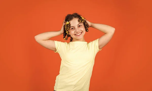 Stijltips. Klein meisje krullen haar met behulp van krulspelden oranje achtergrond. Dochter met krulspelden op haar hoofd lachend. Kapsalon. Vrouwelijke schoonheid routine. Schattig kinderkapsel. Tiener hobby 's — Stockfoto