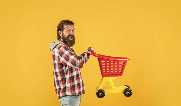 Facet idzie na zakupy. Zabawny człowiek z małym wózkiem. weekend na zakup produktów. cieszy się z pomyślnych zakupów. Brutalny, dojrzały hipster idzie na zakupy. Czas napełnić wózek. — Zdjęcie stockowe