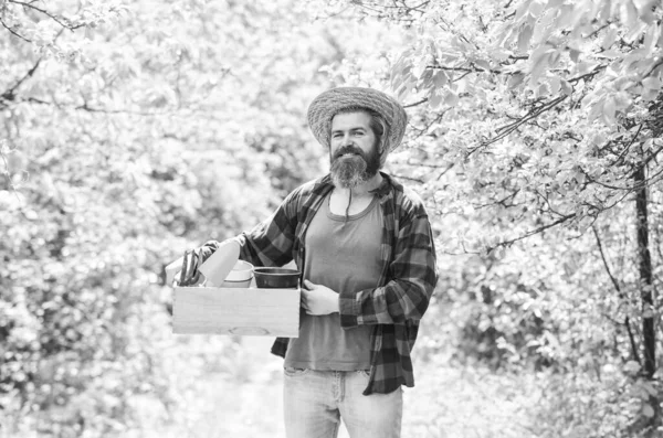 Eco farm. mature man gardener working in greenhouse. brutal male carry garden tools. human and nature. farming and floral concept. spring season. bearded farmer in straw hat with wooden box — Stock Photo, Image