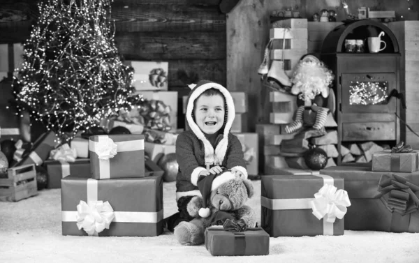 Co jest w środku. Mały chłopiec podekscytowany teraźniejszością. Dzieciak trzyma dekoracyjną piłkę. niedźwiedź zabawka prezent na Boże Narodzenie. Wesołych Świąt. Szczęśliwego Nowego Roku. Szczęśliwy kapelusz Świętego Mikołaja. syn gotowy do świętowania ferii zimowych — Zdjęcie stockowe