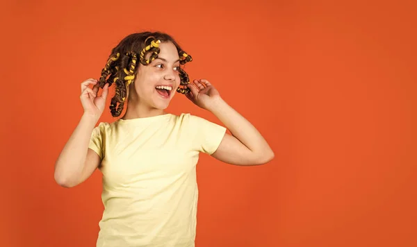 Dicas de estilo. Menina pequena Curling Cabelo Usando Curlers fundo laranja. Cabelo de criança adorável. Passatempos adolescentes. Filha com rolos na cabeça a rir. Salão de cabeleireiro. Rotina de beleza feminina — Fotografia de Stock