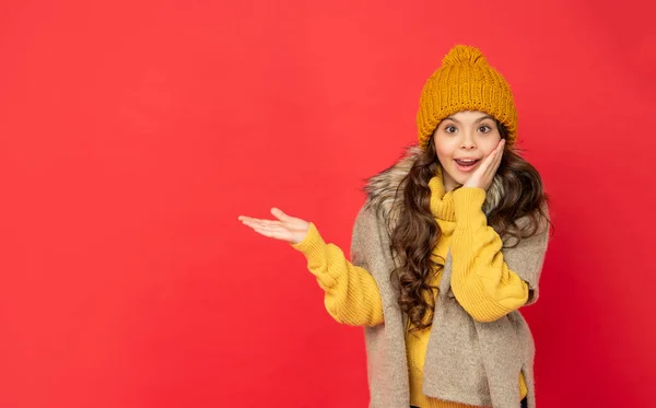 Здивована дитина в трикотажному зимовому капелюсі, що представляє продукт на копіювальному просторі, реклама — стокове фото
