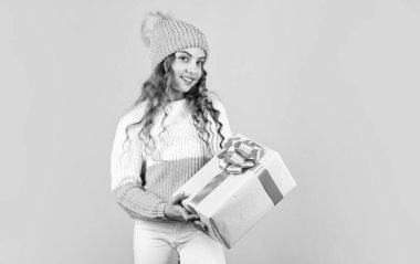 Noel, memnun etme zamanıdır. neşeli küçük kız örgü şapka ve kazak. Çocuk hediye kutusunu yeşil duvarda tutuyor. Mutlu yıllar. Xmas hediye alışverişi. Sana da mutlu noeller. Kış tatili indirimleri