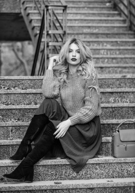 Giyilebilir trendler. Kız eteğinin üstüne daha büyük bir katman örülmüş. Sonbahar formülü. Sonbahar için stil süveter ve etek karışımı. Muhteşem kadın saç stili merdivenlerde oturuyor. Ilık sonbahar. Sonbahar moda trendi