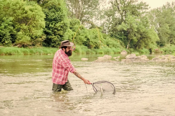 Reel Sport fishing. mature man fly fishing. man catching fish. hobby and sport activity. pothunter. summer weekend. Big game fishing. bearded fisher in water. fisherman with fishing rod