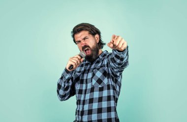 Parti performansı. Sakallı hippi mikrofonda şarkı söylüyor. Mikrofonlu adam. Müzik konsepti. Kareli gömlek giyen şarkı söyleyen adam. Karaoke kulübünde kendine güvenen erkek şarkıcı