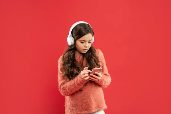 Niño ocupado en suéter escuchar música en los auriculares y mensajes en el teléfono inteligente, la infancia — Foto de Stock