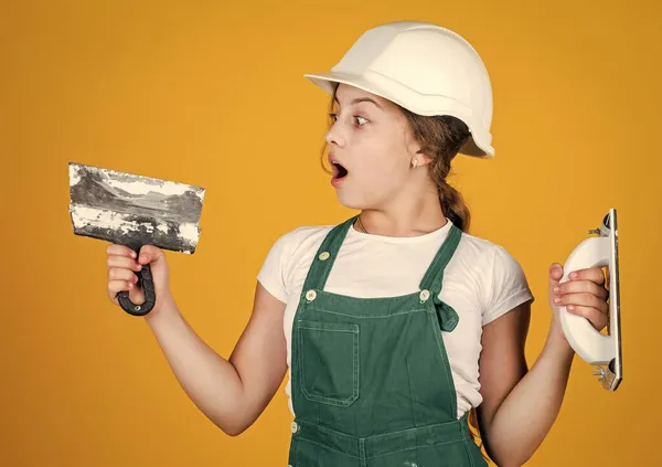 ああ私の神。へらを持つ幸せな小さな建設の女の子。10代の女の子はパテナイフを使う。カバーとヘルメットにヘラで作る。子供の修理用の壁に貼り付けてある。自宅の改装。道具付きの子供 — ストック写真